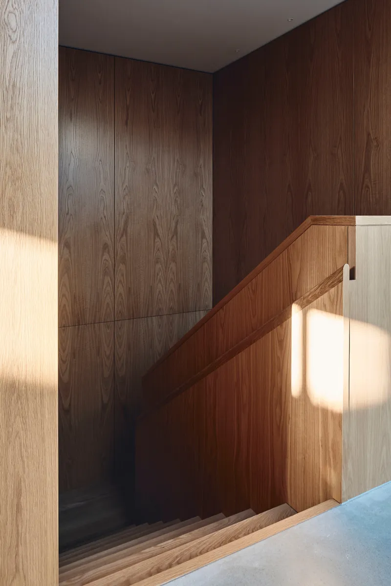 Stairwell with two-tone wood paneling and sunlight casting shadows across the balustrade