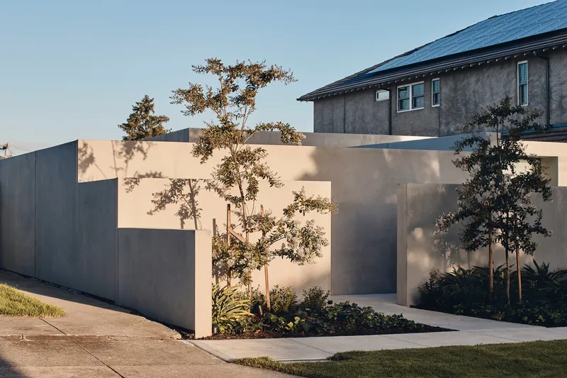 Stepped concrete entry wall with planted trees casting shadows in afternoon light