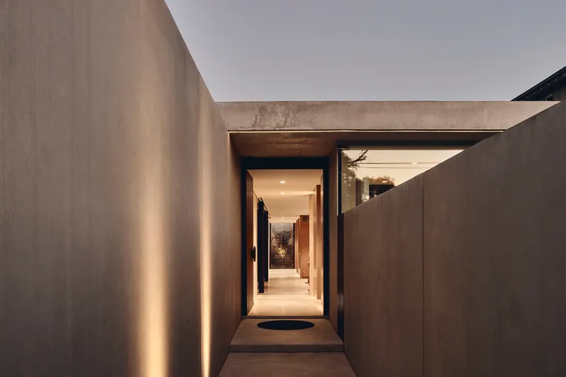 Entry passage framed by concrete walls with vertical lighting slots at twilight