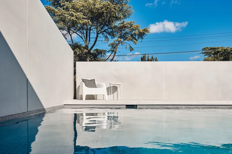 Pool terrace with white chairs reflected in still water under a clear blue sky