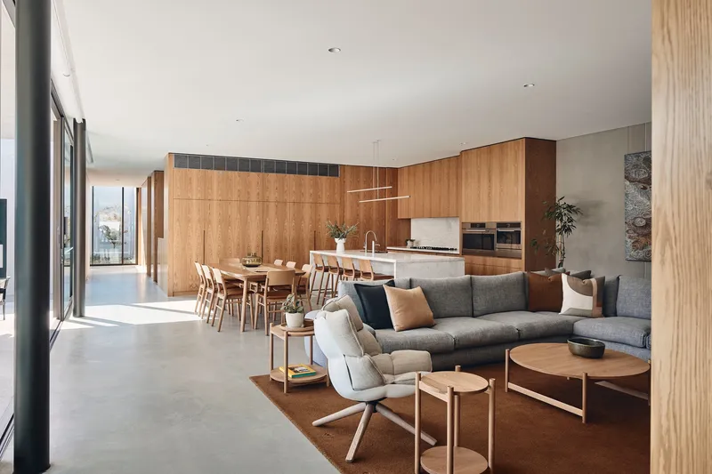 Open-plan living area with timber cabinetry and polished concrete floor beneath a white ceiling