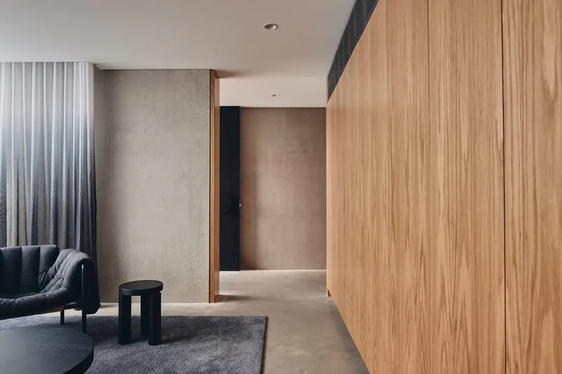 Timber-clad corridor with concrete walls and grey curtains beside a seating area