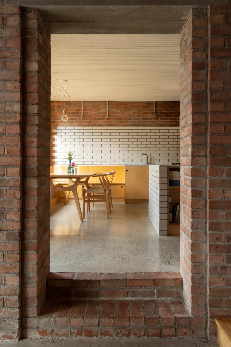View through brick portal into dining area with white tile backsplash and pendant lighting