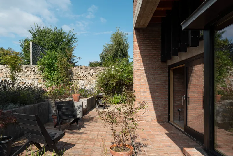 Brick paved terrace with potted trees and black timber seating against a stone boundary wall