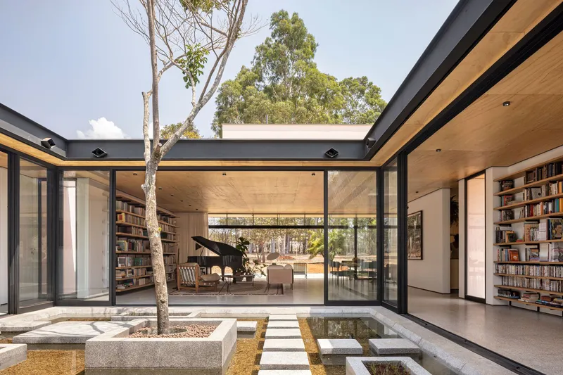 Internal courtyard with concrete planter bed, stepping stones over water, and glazed pavilions with timber ceilings