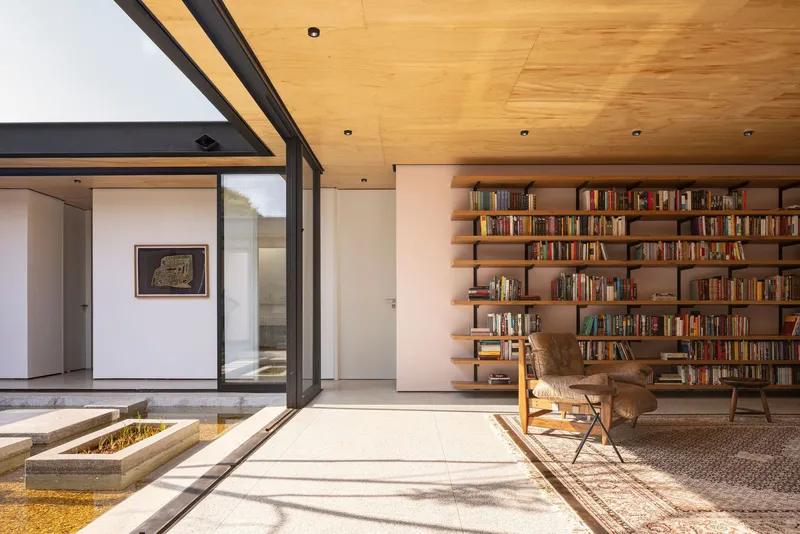 Courtyard view of timber bookshelves and reading chair with plywood ceiling and concrete paving slabs