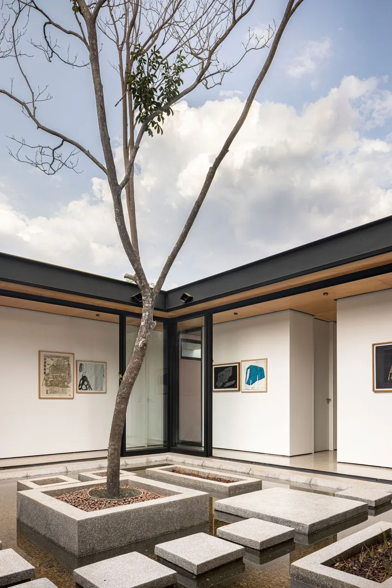Courtyard corner showing concrete planter with tree, stepping stones, and gallery walls under cloudy sky