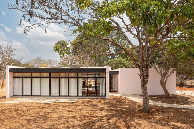 Street facade with horizontal timber louvers and black-framed glazing under overhanging roof amid mature trees