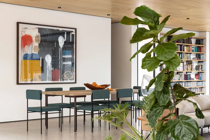 Dining area with round timber table and built-in bookshelves framed by a fiddle-leaf fig tree