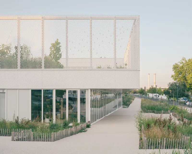 Pedestrian path alongside the mesh-screened upper terrace and glazed ground floor with planted beds behind timber fencing