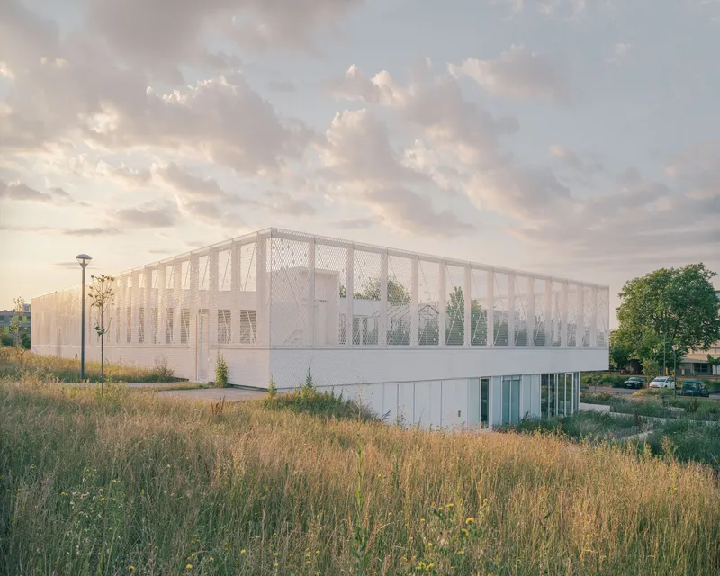 Two-story volume with expanded metal mesh facade surrounding the upper floor at dusk among wildflower meadow