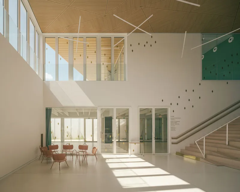 Double-height interior foyer with timber-clad ceiling, wide staircase and linear light fixtures casting shadows on white walls