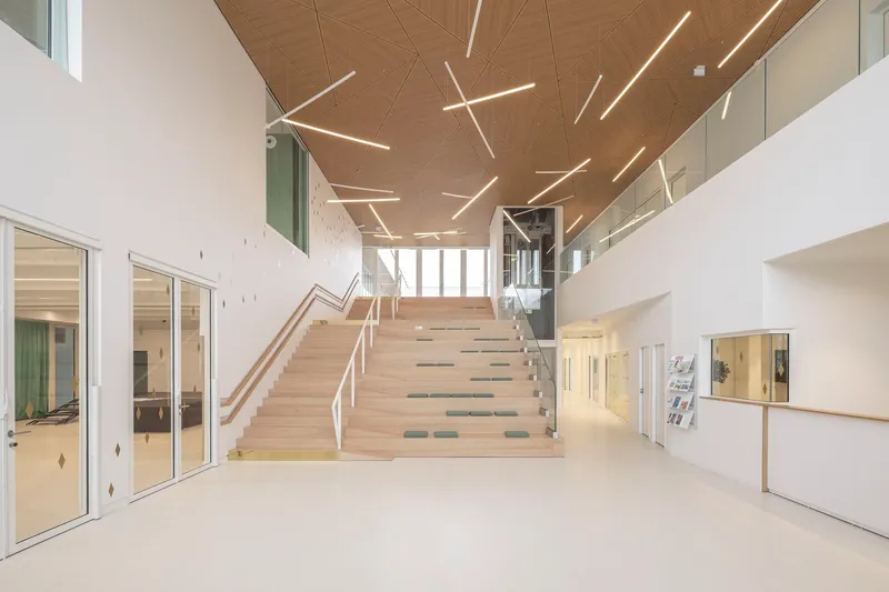 Central timber staircase ascending beneath a wooden ceiling with geometric linear lighting fixtures in the entrance hall