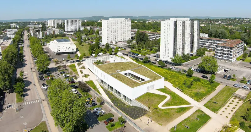Aerial view showing the rectangular building with green roof courtyard surrounded by residential towers and tree-lined streets
