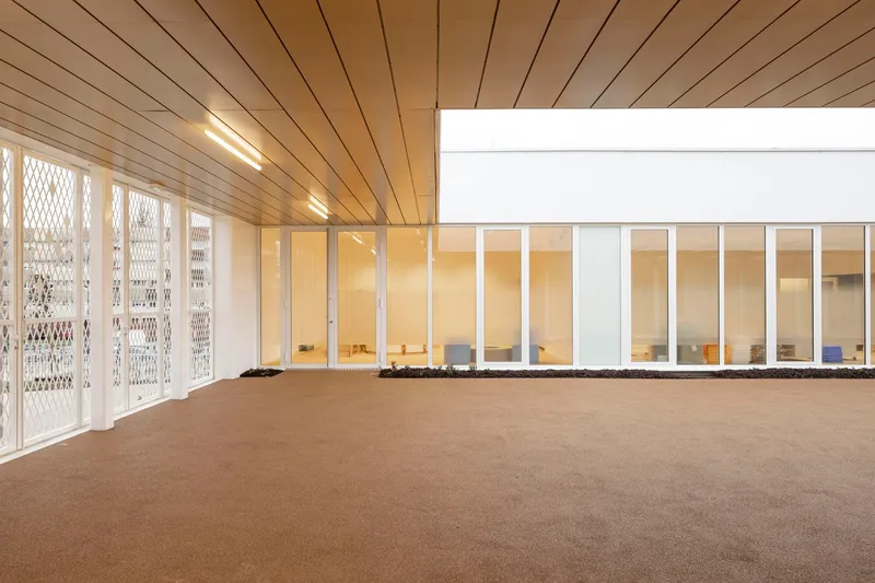 Interior room with timber plank ceiling and perforated metal doors opening to a glazed corridor