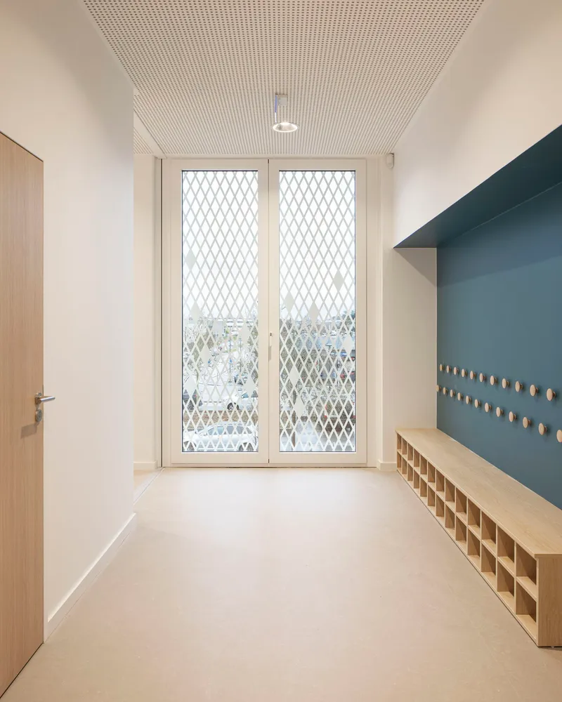 Entry corridor with plywood bench, blue pegboard wall and diamond mesh glazed doors
