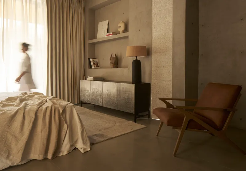 Bedroom with floating shelves and person passing through soft natural light from sheer curtains