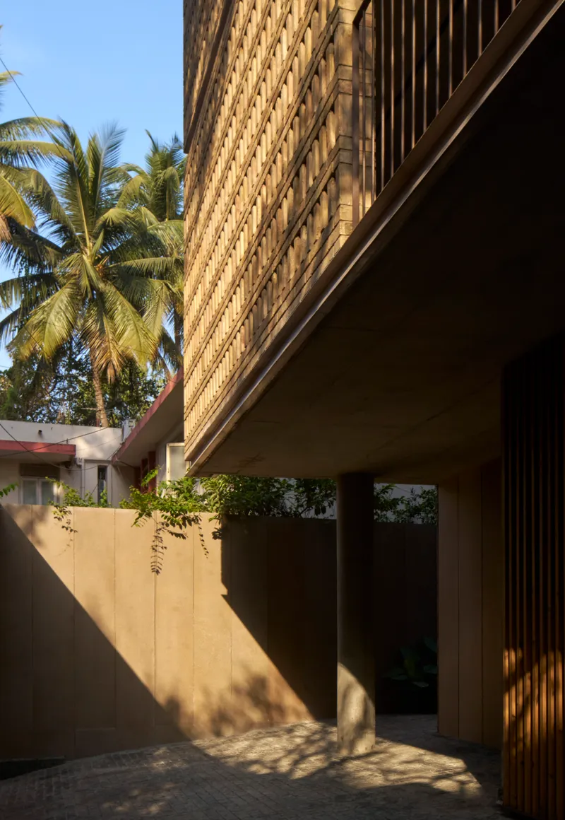 Entry courtyard with smooth concrete wall and perforated brick screen above framed by palm trees