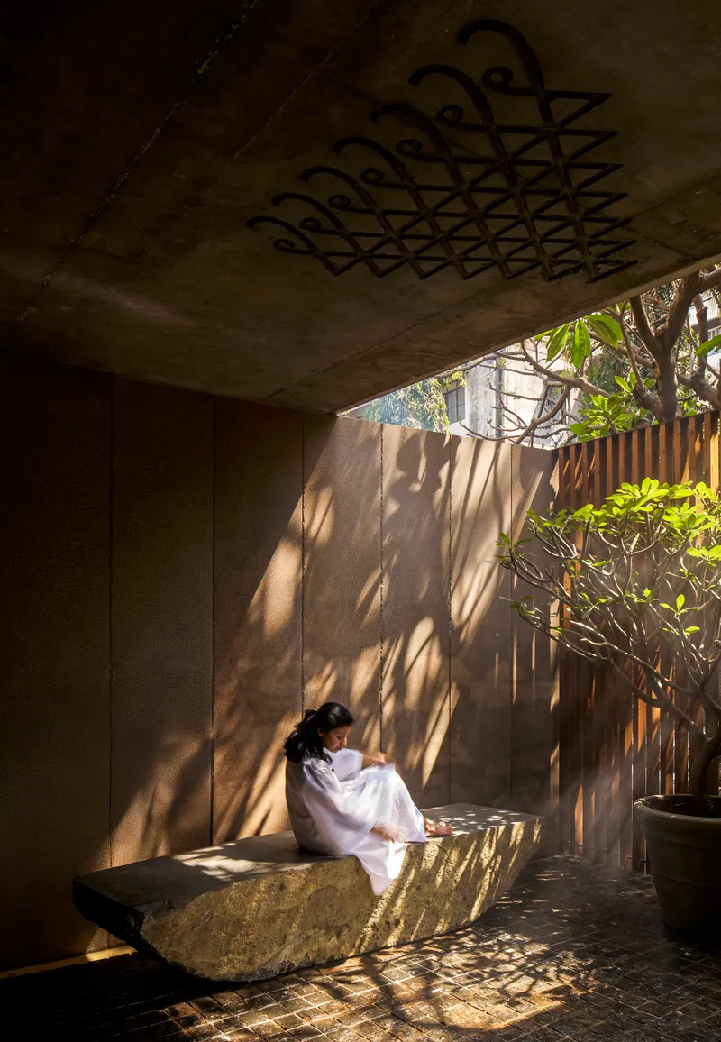 Corner of shaded courtyard showing dappled light on concrete wall with seated figure on stone bench