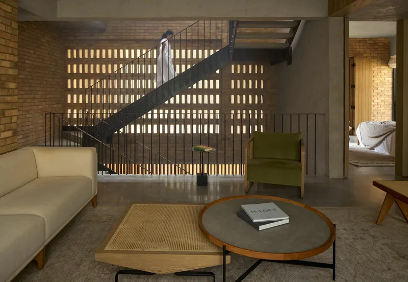 Living room with steel staircase rising against backlit perforated brick screen wall at night