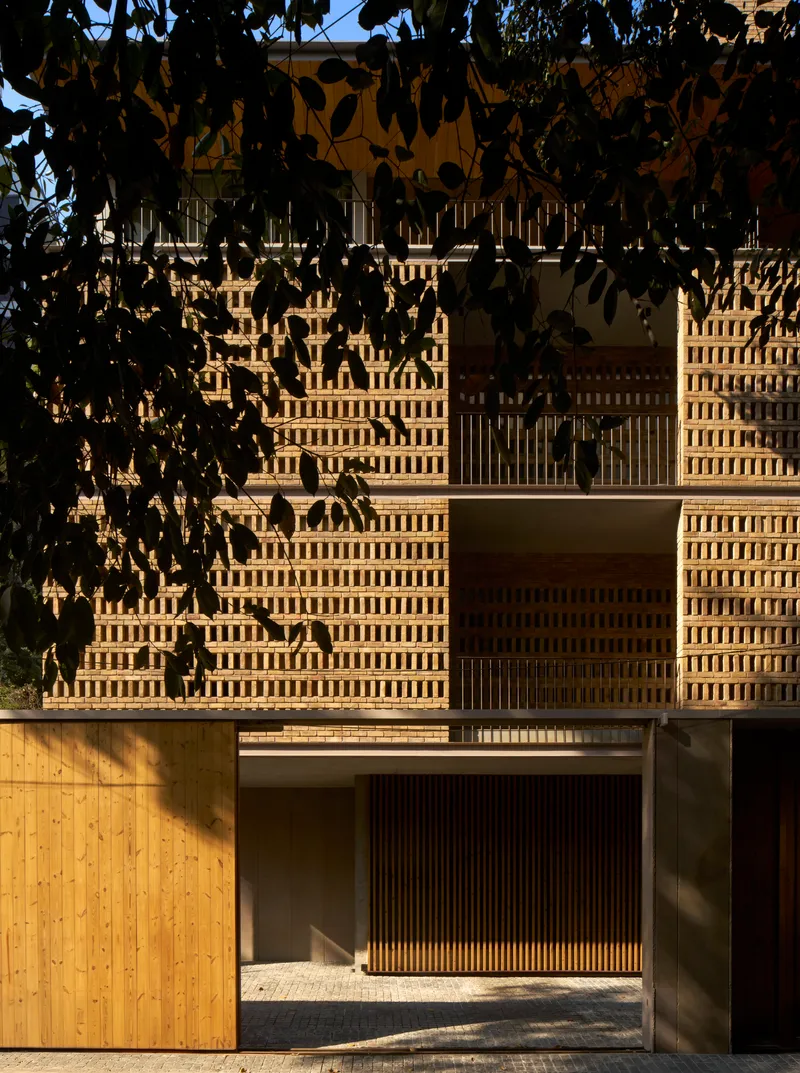 Entry view showing perforated brick screen walls and timber base filtered by tree shadow
