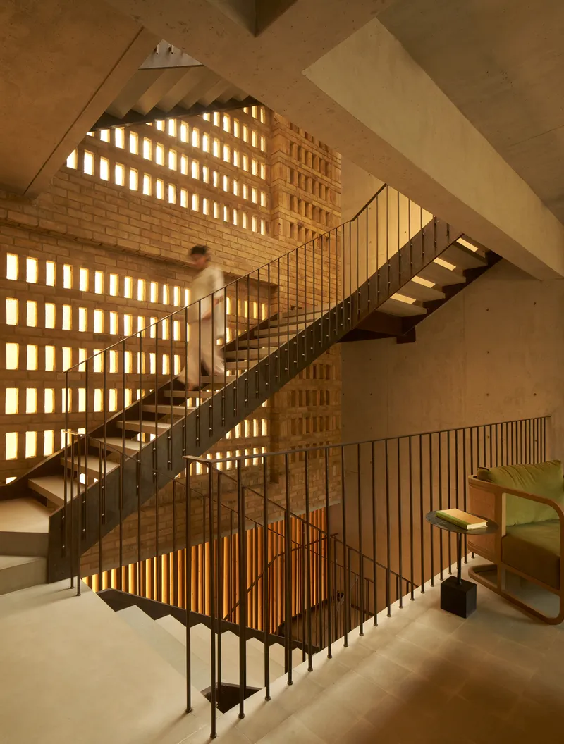 Central stairwell with steel and timber stair illuminated by backlit perforated brick walls