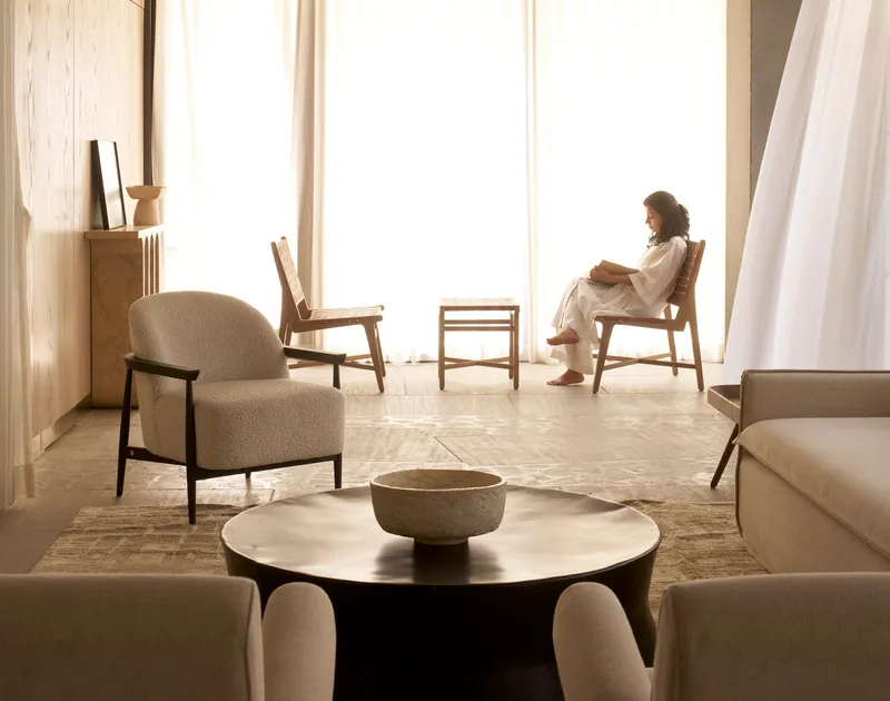 Living space with seated figure by floor-to-ceiling windows in soft daylight