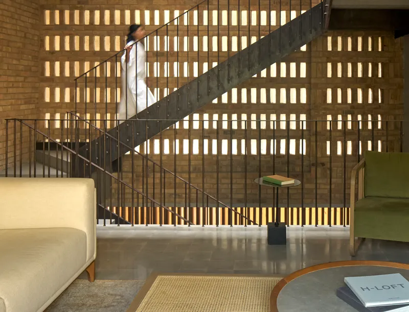 Curved steel staircase rising against brick wall with backlit vertical openings
