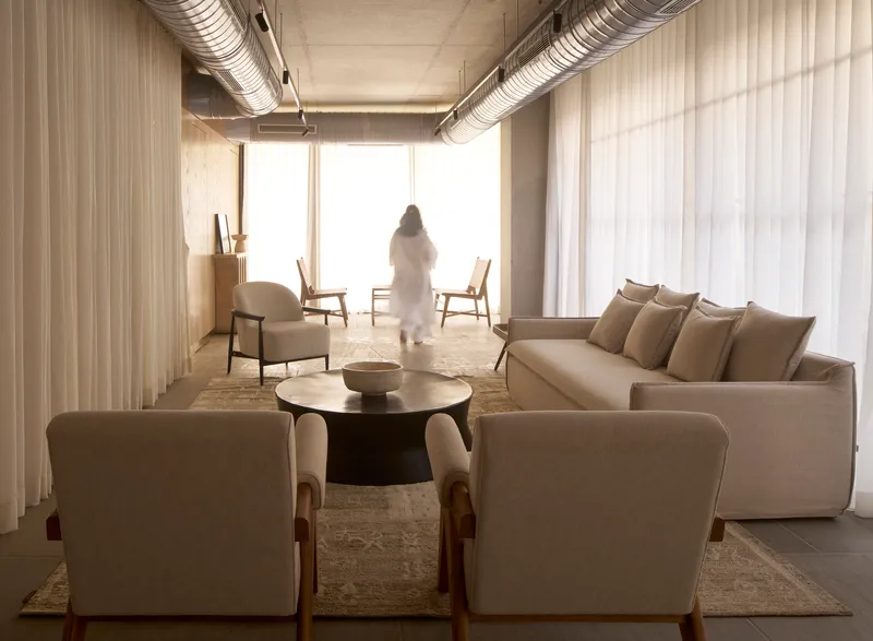 Living area with exposed ceiling ducts, sheer curtains and a figure silhouetted against bright windows