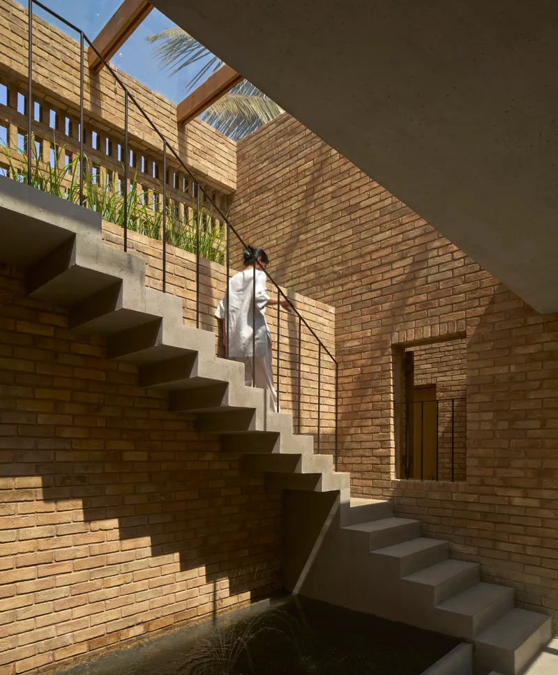 Concrete staircase rising through a brick courtyard with clerestory openings and a figure ascending