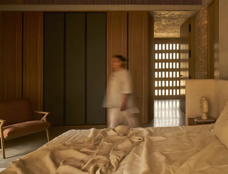 Bedroom with gridded brick screen wall and blurred figure walking through doorway at dusk