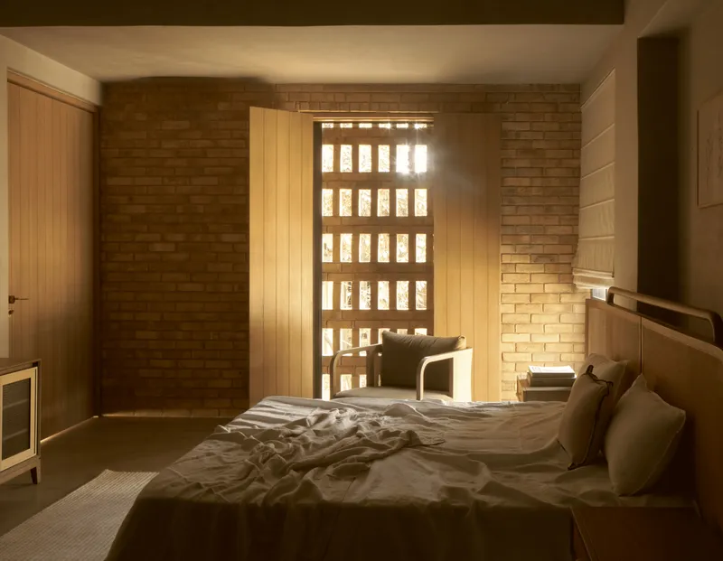 Bedroom with perforated brick screen window casting patterned light across bed and floor