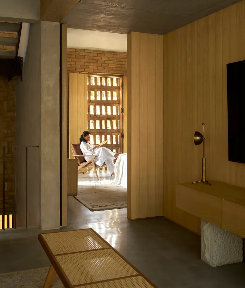 View through timber-lined hallway toward seating alcove with gridded brick light screen