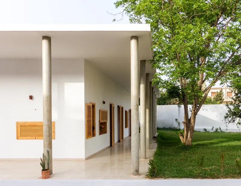 Covered porch with cylindrical concrete columns and wood shutters opening to lawn with trees