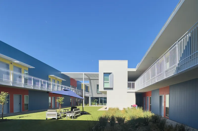 Courtyard view framed by white corrugated volumes and double-loaded corridors with outdoor benches on grass