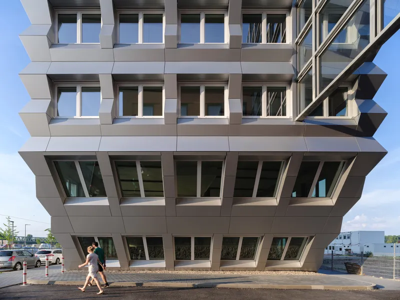 Close view of the cantilevered ground floor with angled window frames and pedestrians walking beneath