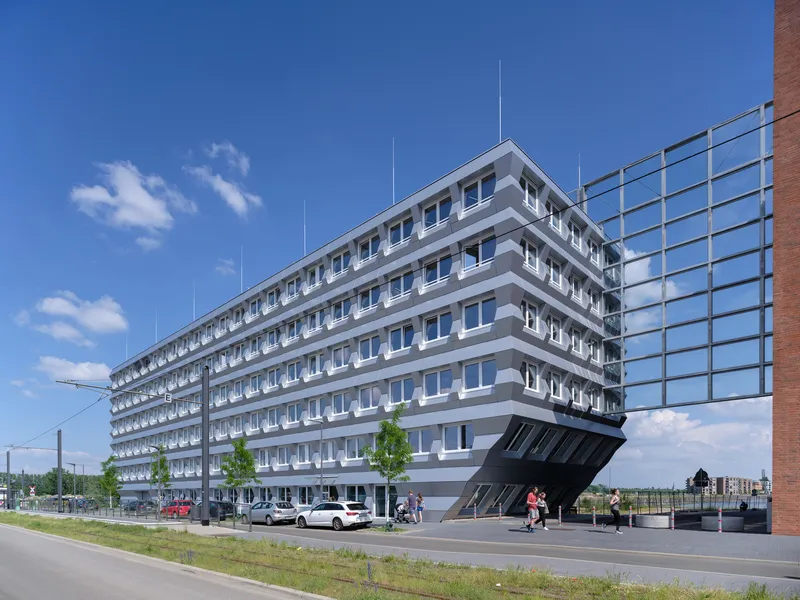 Street view of the horizontal layered facade with cantilevered base and cyclists passing on a clear day