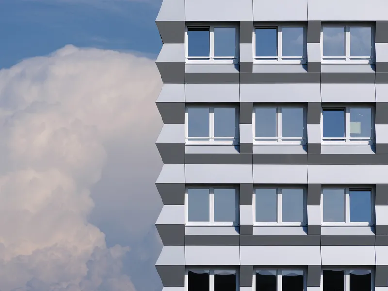 Corner detail of the white panel facade with inset windows against a cloudy blue sky