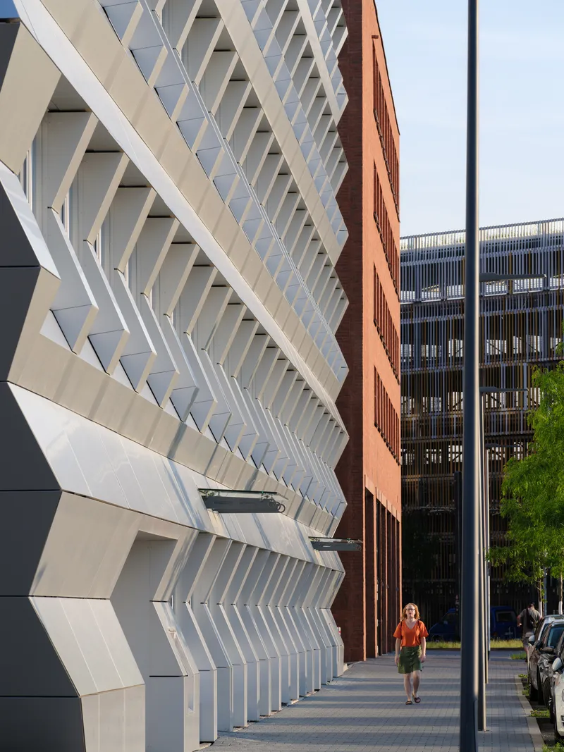 Angled sunscreen louvers on the white facade with a pedestrian walking beneath the shaded sidewalk