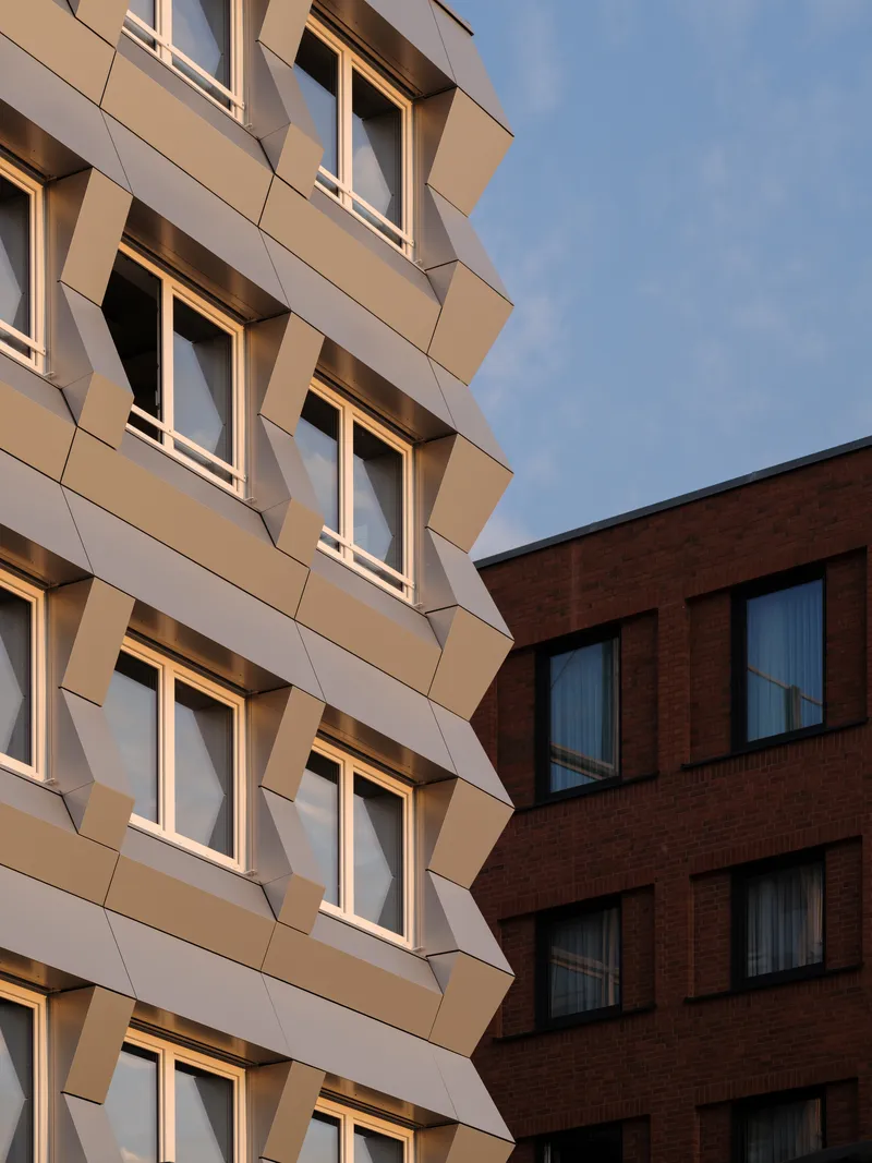 Faceted white facade meeting a brick volume in warm evening light