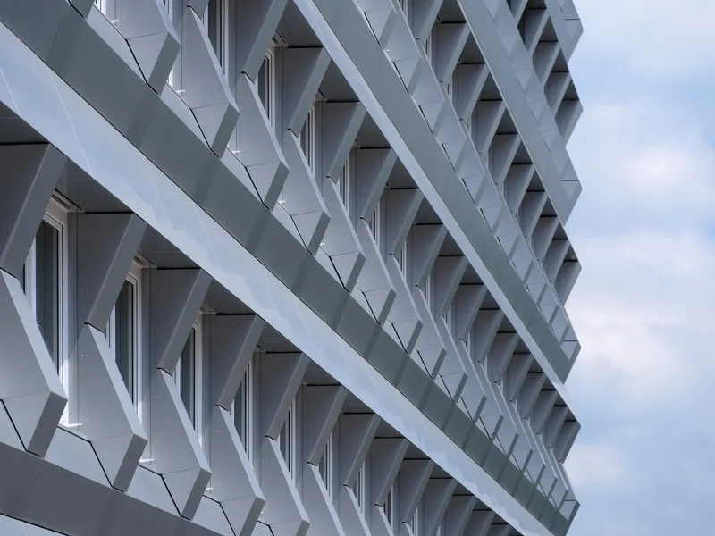 Close-up of the white diagonal brise-soleil lattice forming triangular shadows across recessed balconies under cloudy skies