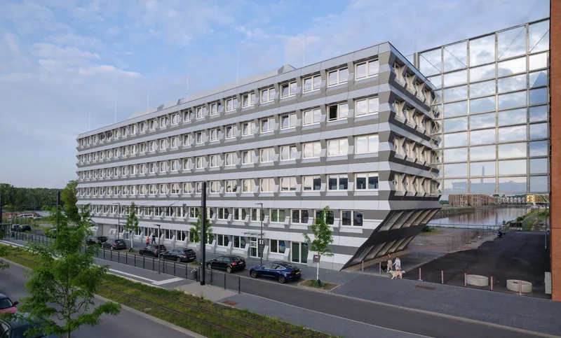Street view of the repetitive window facade with young street trees and parked cars below