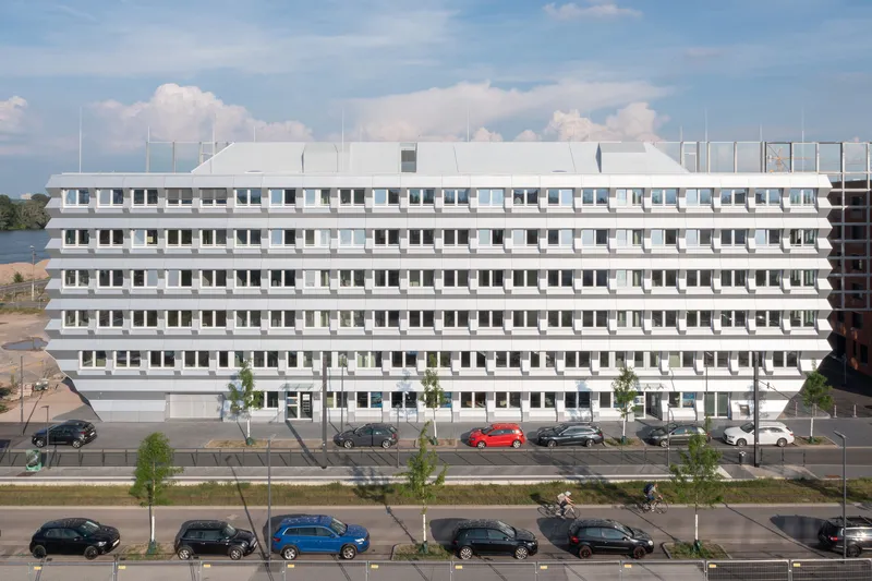 Long elevation showing horizontal banding of white panels and recessed windows under cloudy skies