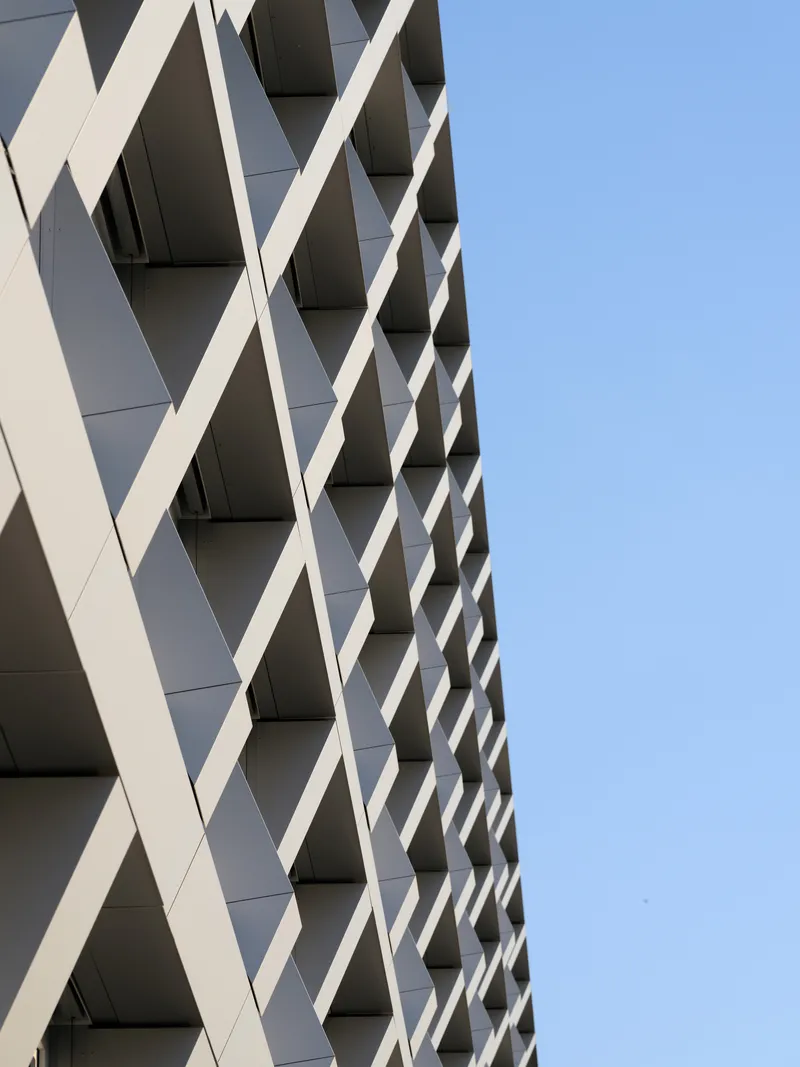 Angled view of the crisscrossing white facade fins creating a diamond pattern against clear blue sky
