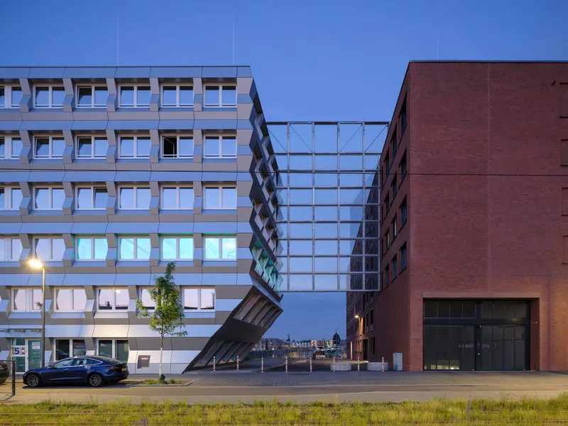 Street view at twilight showing the cantilevered entrance volume connecting the latticed tower and glass curtain wall