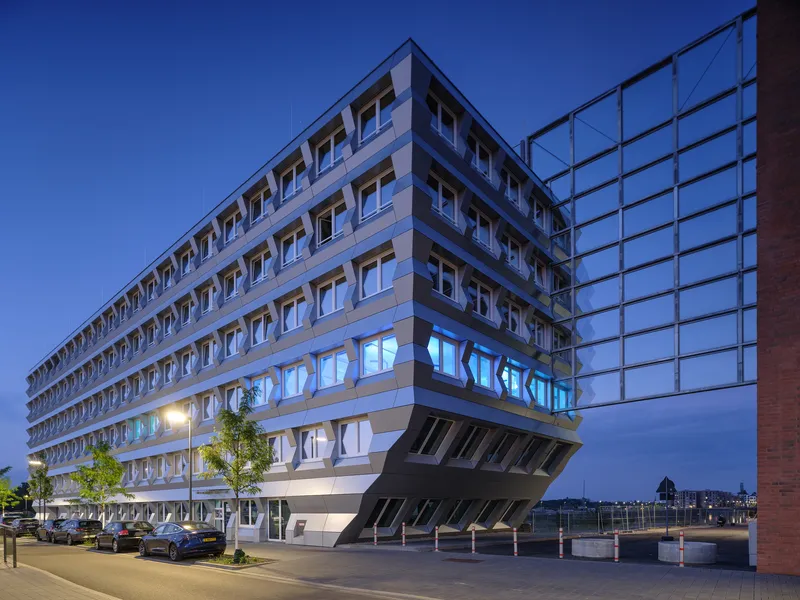 Full facade at blue hour with illuminated ground floor and parked cars along the tree-lined street