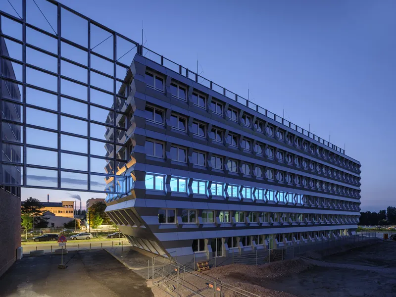 Night view showing the reflective glass curtain wall beside the horizontal window bands and cantilevered base