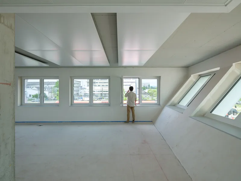 Interior with angled skylight and windows where a person stands gazing at the urban view