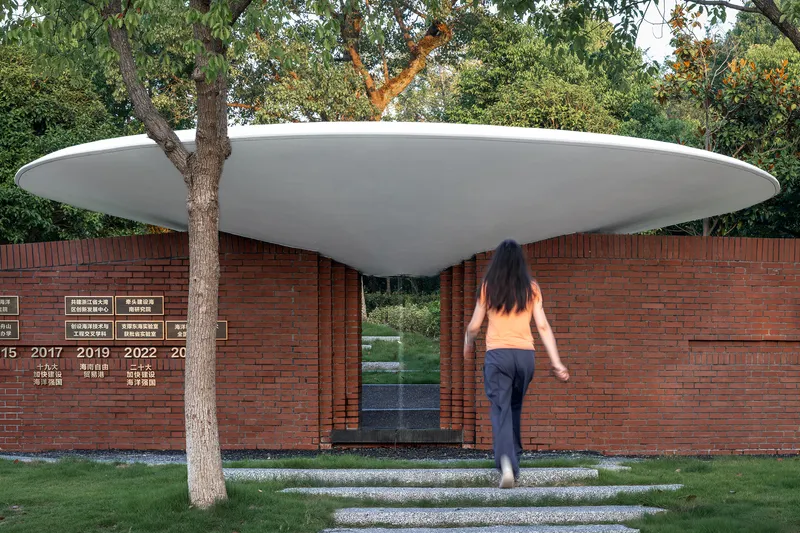 Red brick wall memorial with white disc roof canopy and visitor approaching along grass path