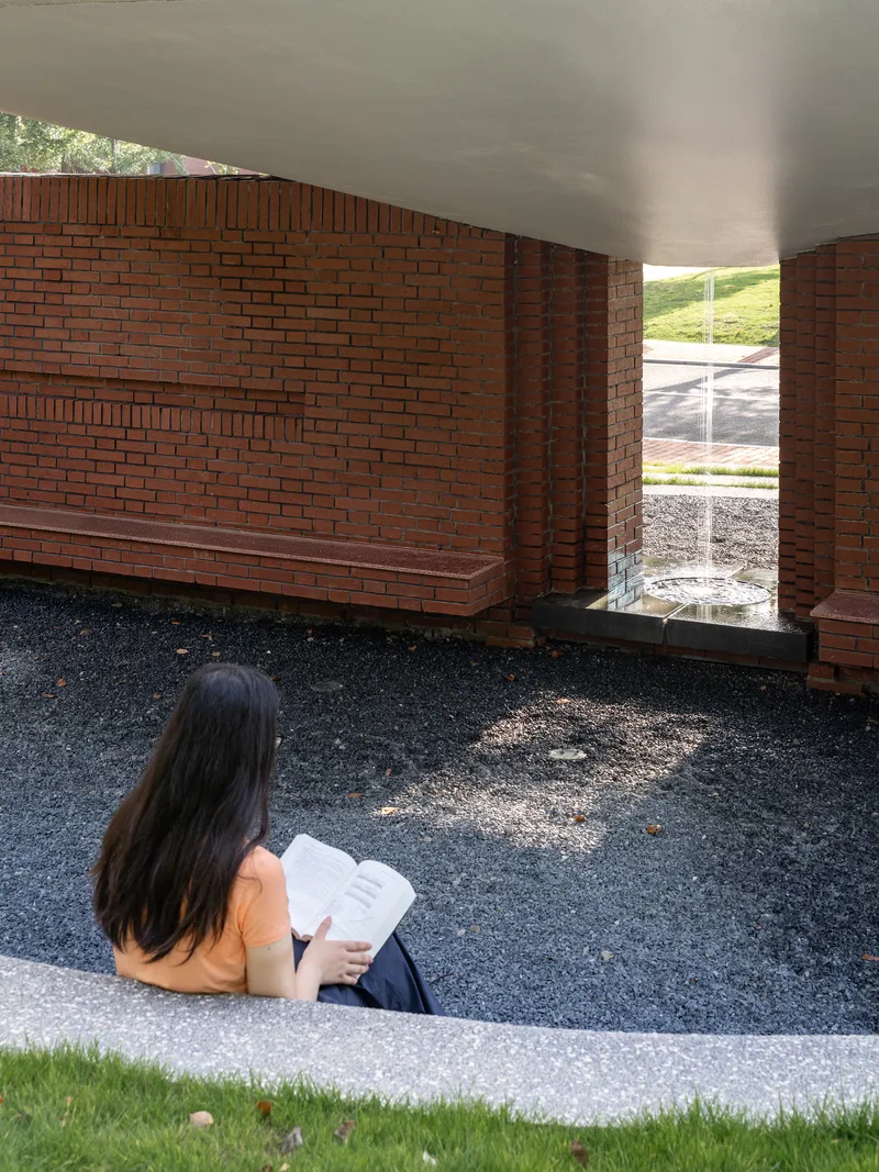 Interior courtyard with red brick walls and seated visitor reading beneath smooth white ceiling
